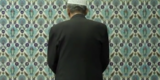 Ein Mann steht betend vor einer Wand in einer Moschee.