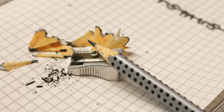 Ein Bleistift und ein Spitzer liegen auf einem Notizbuch.